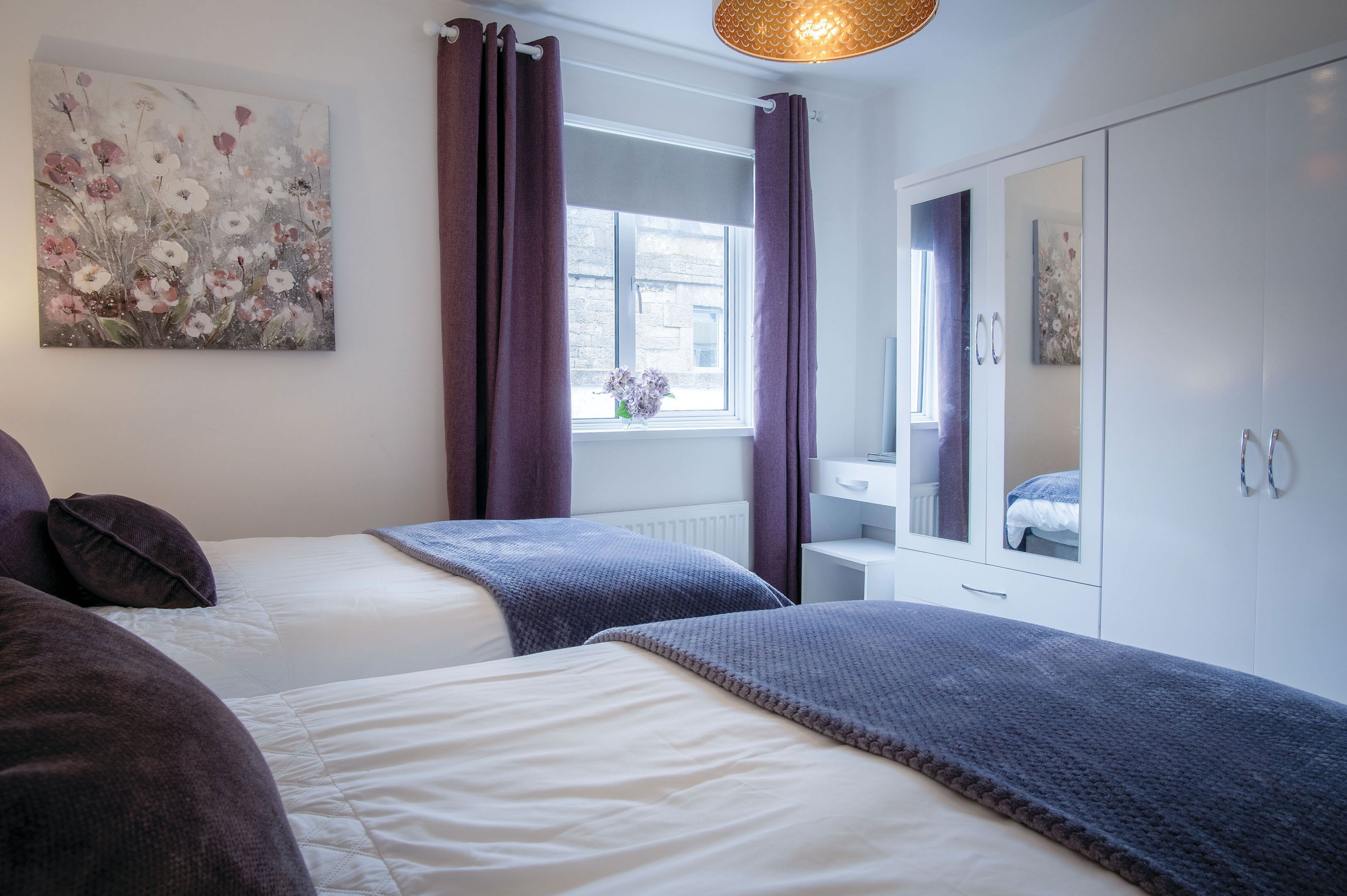Una camera da letto con due letti, una finestra con tende, un termosifone, un armadio e un quadro appeso al muro.