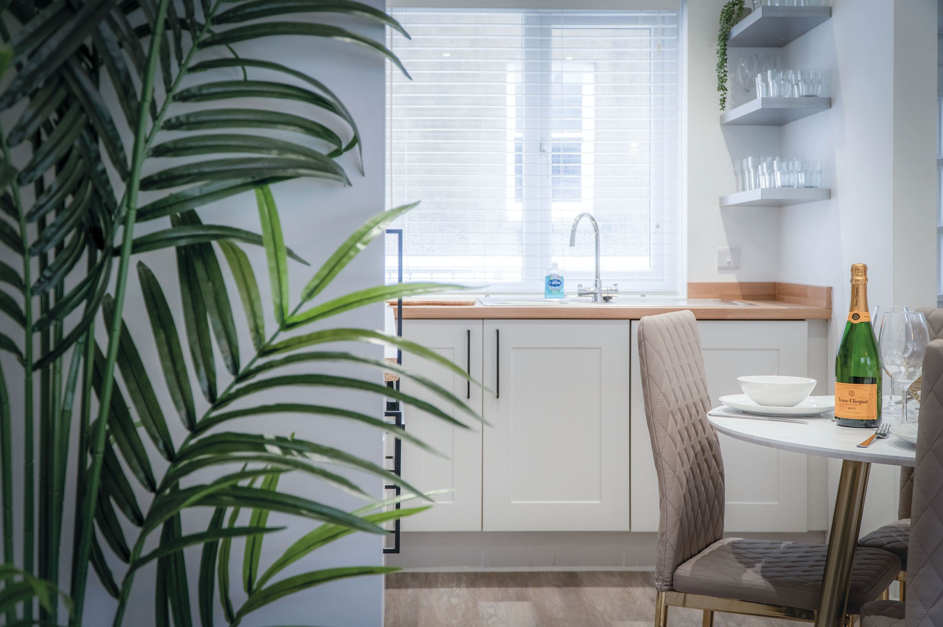 A modern kitchen with white cabinets, a sink, and a dining area with a table and chairs.