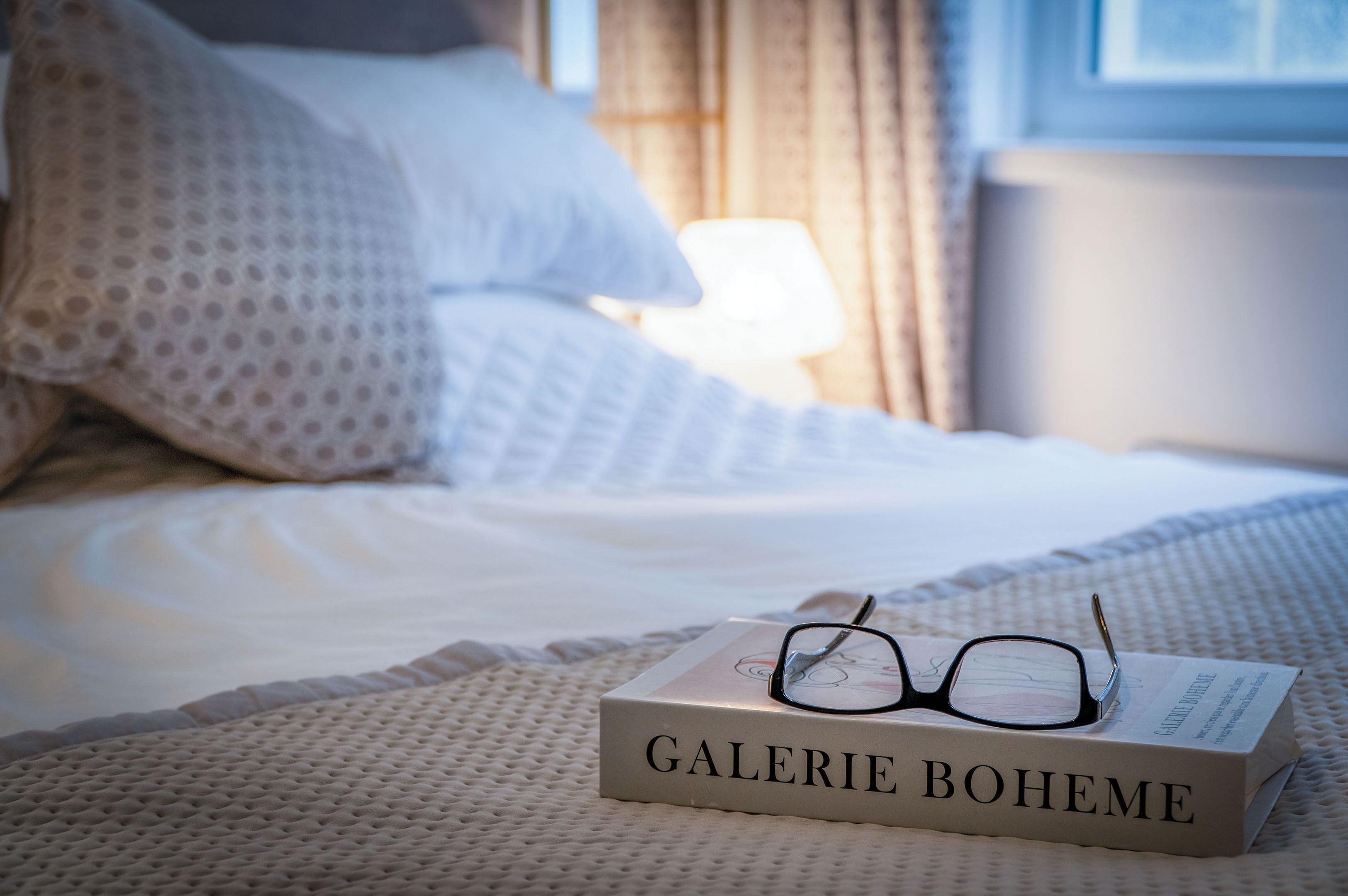 Egy ágy, rajta egy „GALERIE BOHEME” című könyv és egy szemüveg.
