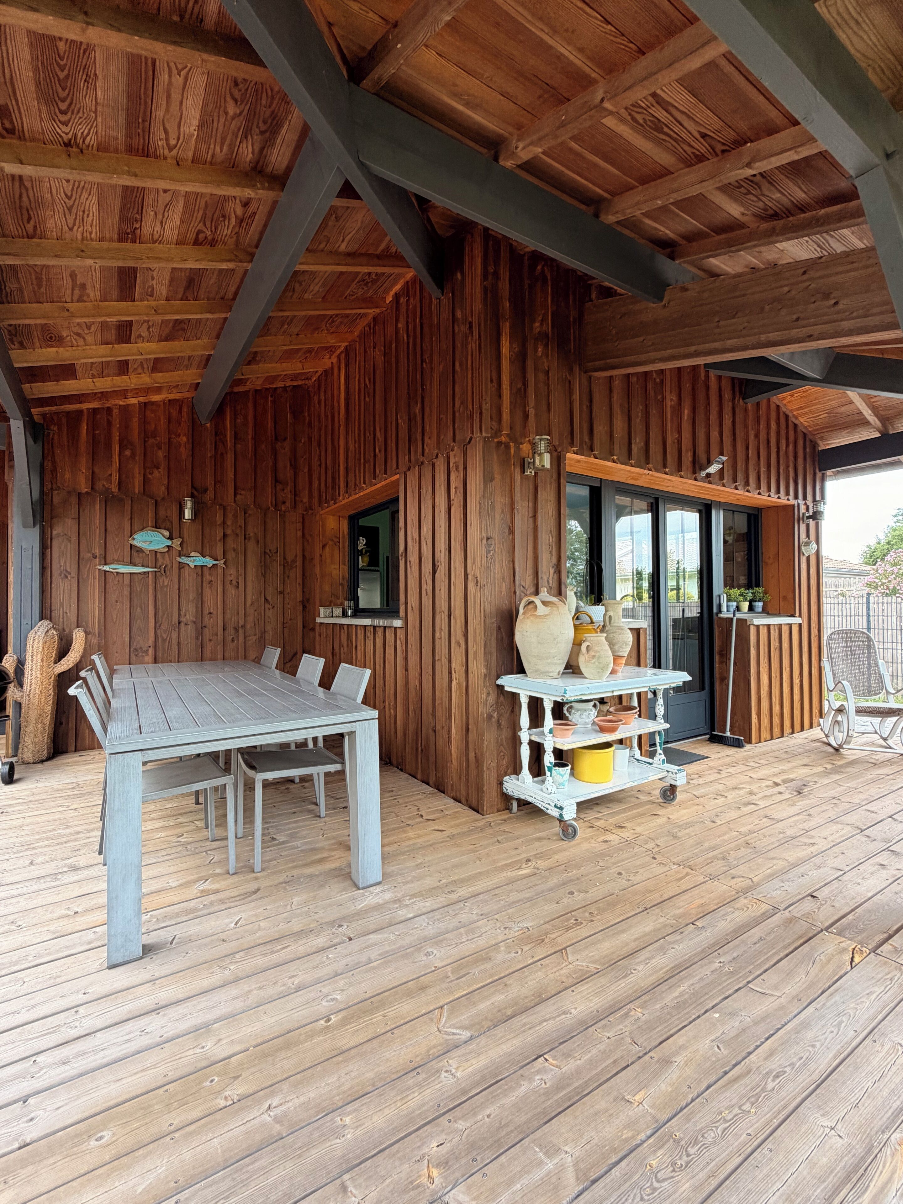 Ein Holzinterieur mit Tisch und Stühlen, ein Wagen mit Keramik und einer Kakteen-Dekoration.