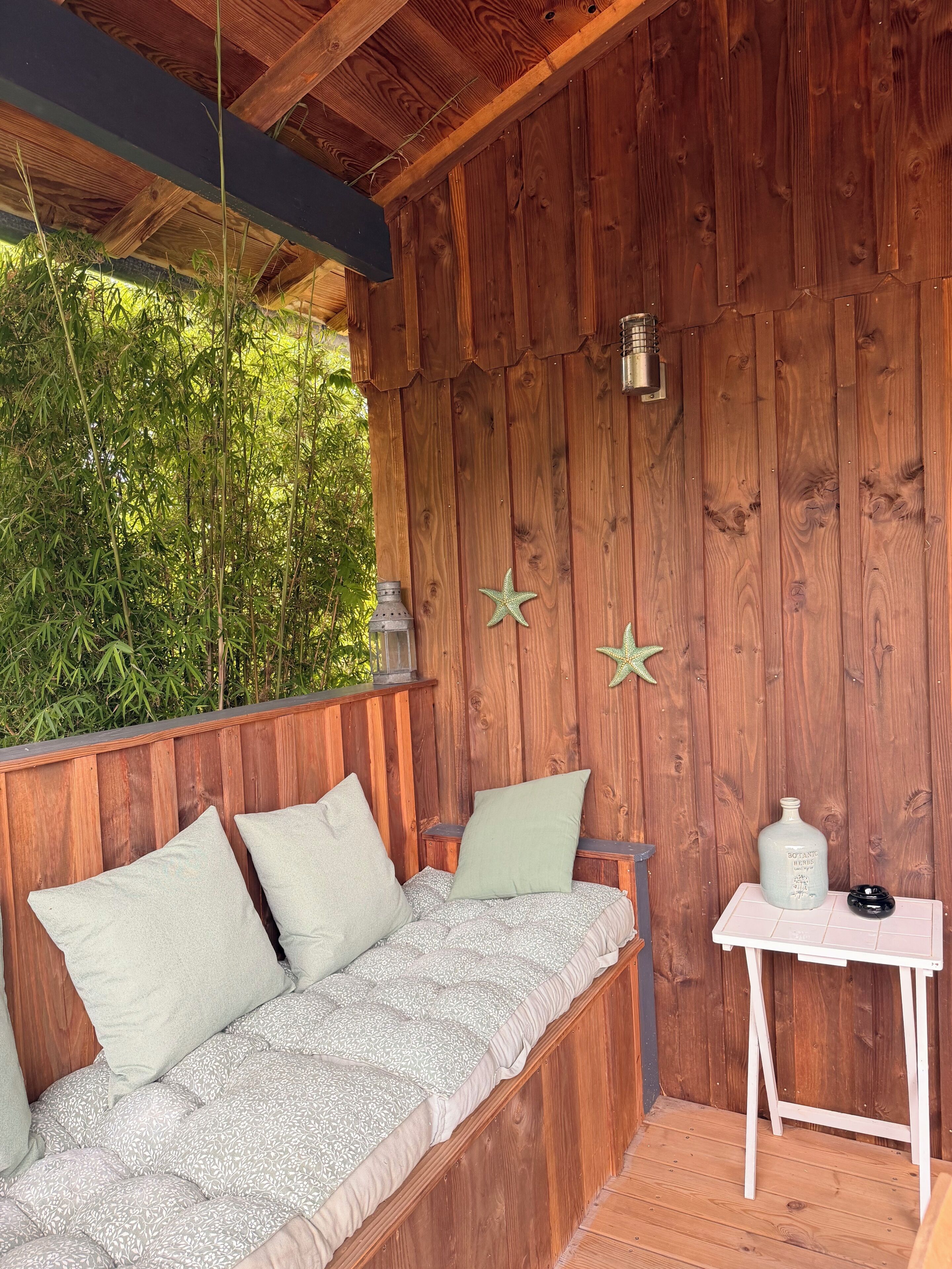 A wooden deck with a bench and a small table, surrounded by bamboo plants.