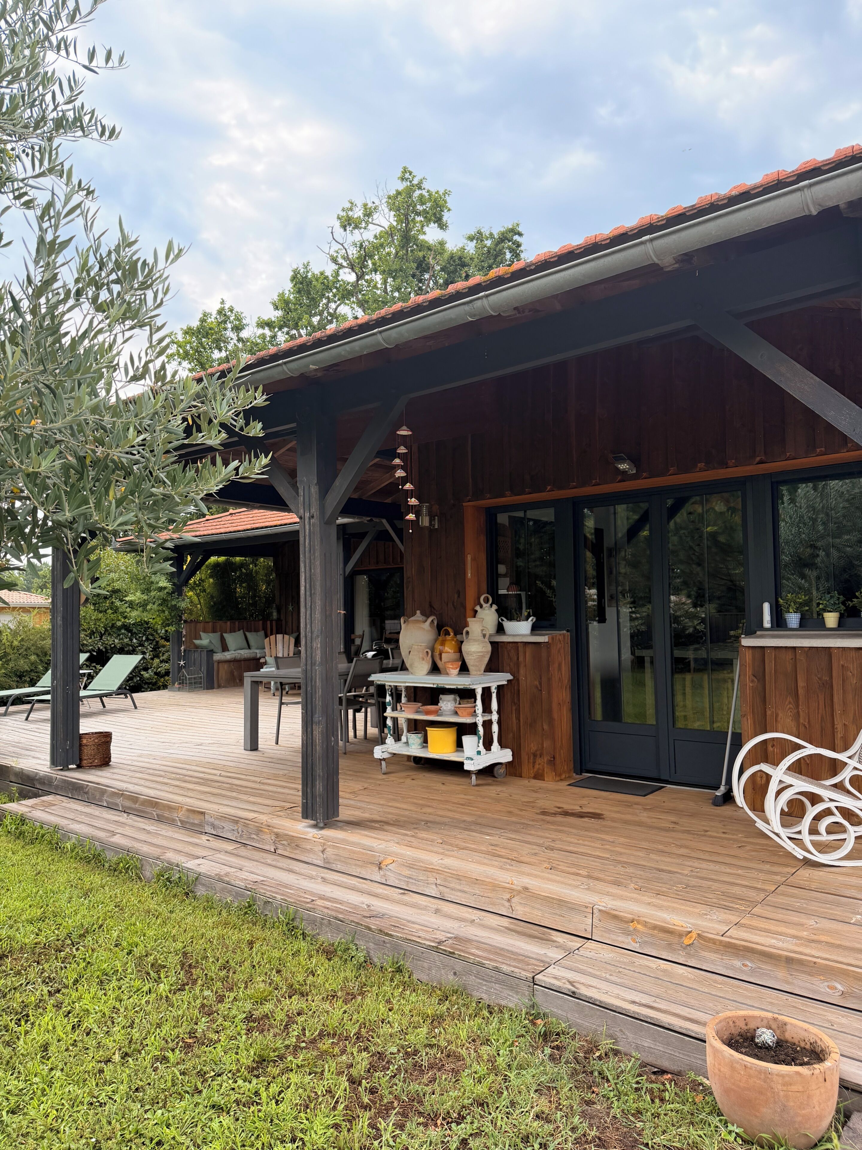 Een overdekt terras buiten, met een houten terras, een tafel met keramiek en een zithoek.