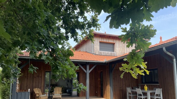 Una casa de madera con techo de tejas, un porche cubierto y mobiliario exterior.