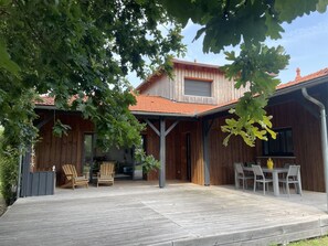 Una casa de madera con techo de tejas, un porche cubierto y mobiliario exterior.
