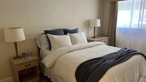 Habitación de hotel con cama, dos mesitas de noche, una lámpara, un reloj y ventana con cortinas.