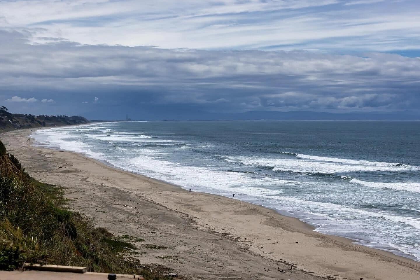 A beach with waves, a sandy shore, and a cloudy sky.