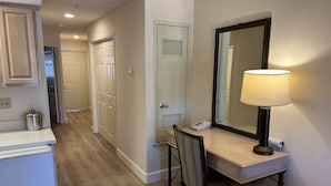 Habitación de hotel con kitchenette, escritorio con lámpara, silla y espejo grande.