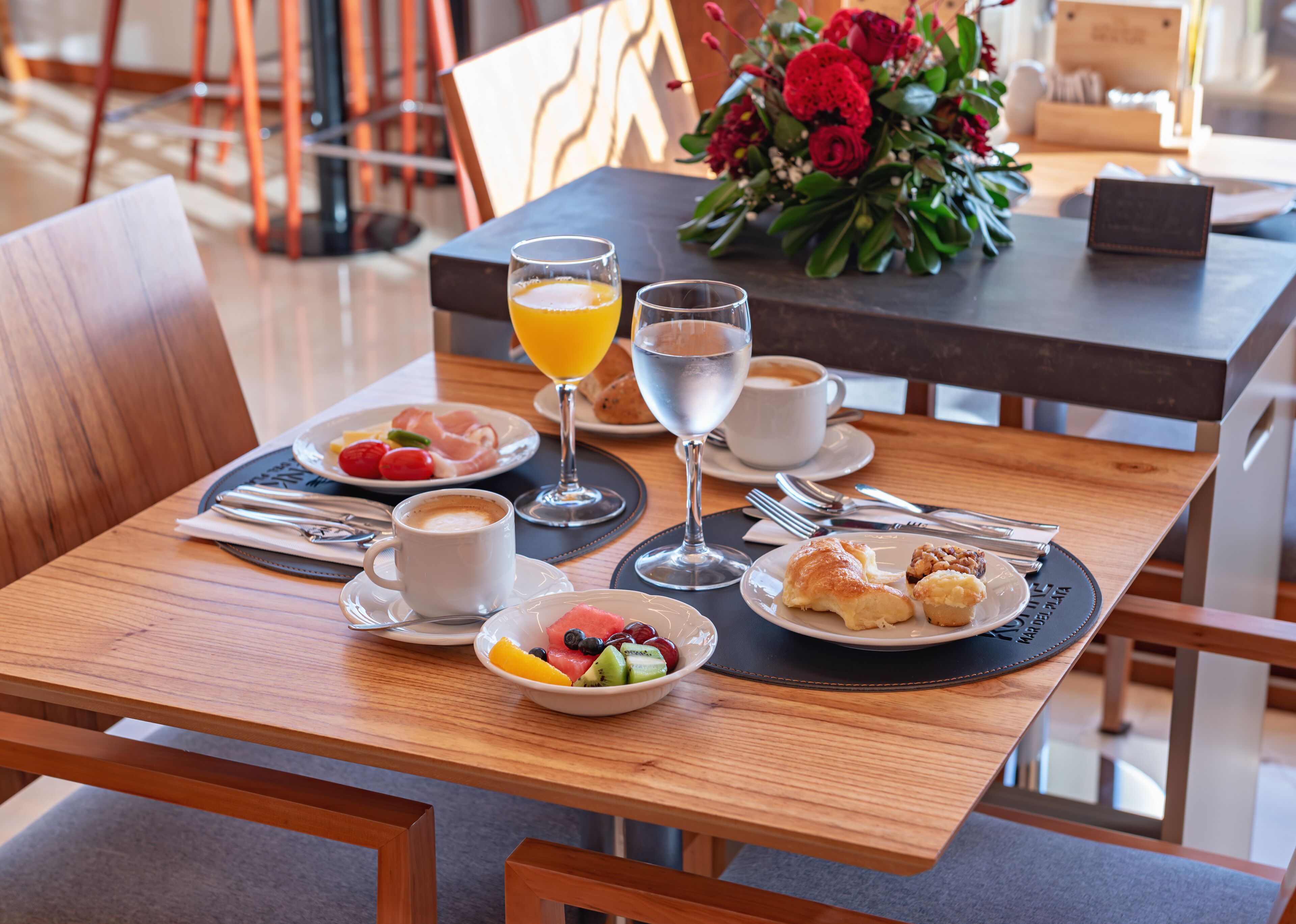 Una mesa de desayuno con platos de comida, un vaso de zumo de naranja, un vaso de agua y una taza de café.