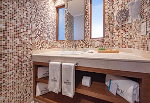 Un baño con paredes de mosaicos, un mueble de tocador de madera, un lavabo, un espejo y toallas con la marca 'KONKE'.