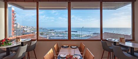 Comedor con una mesa lista para dos, ventanas amplias con vistas al mar y al paisaje urbano.