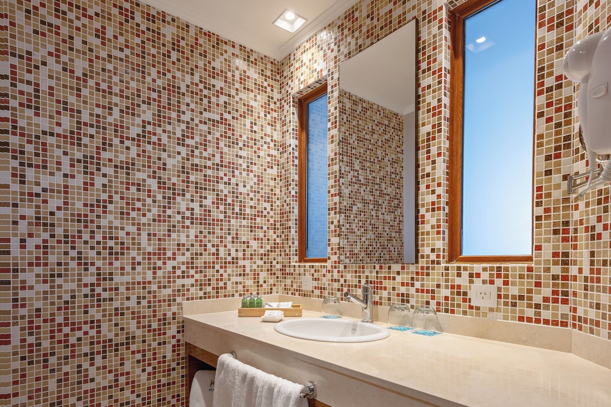 Un baño moderno con paredes de mosaicos, un espejo grande y un mueble de tocador de madera.