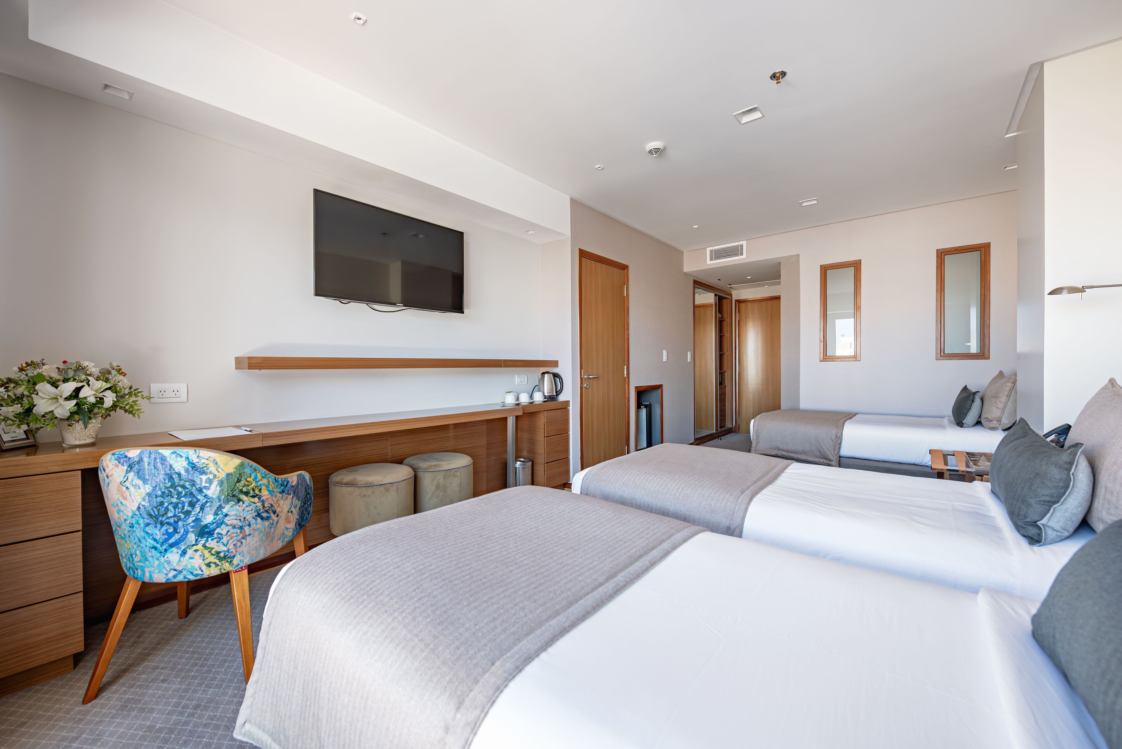 A modern hotel room with two beds, a desk, a chair, a TV, and a bathroom.