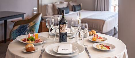 Mesa de comedor de hotel dispuesta con platos, cubiertos, copas y una botella de vino.