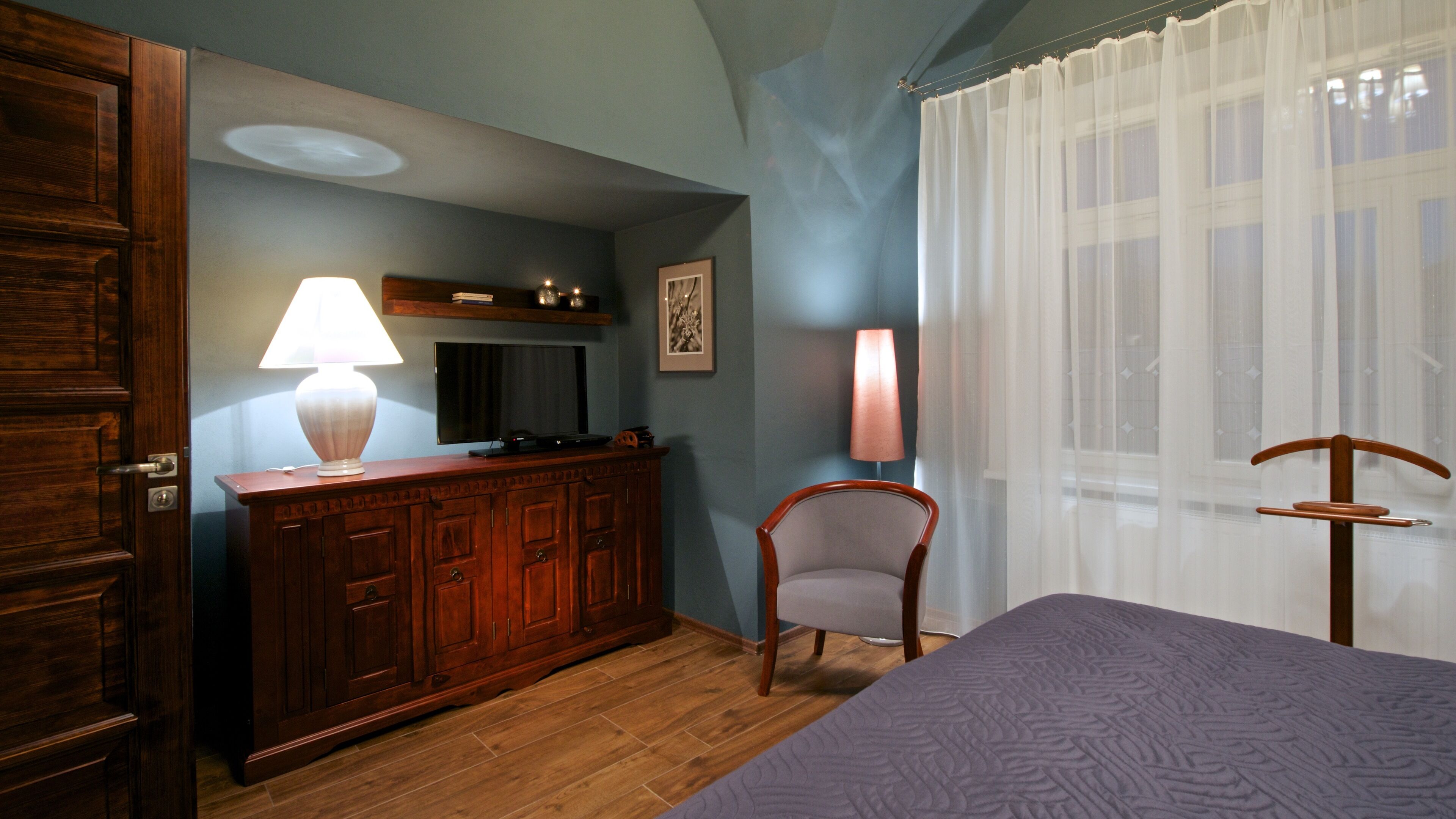 A room with a wooden cabinet, a television, a chair, and a bed.