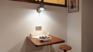Una habitación pequeña y acogedora con una mesa de madera, dos taburetes, una lámpara de pared y un cuadro enmarcado.