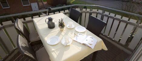 A balcony with a table set for two, including plates, cups, a pitcher, and a notebook.