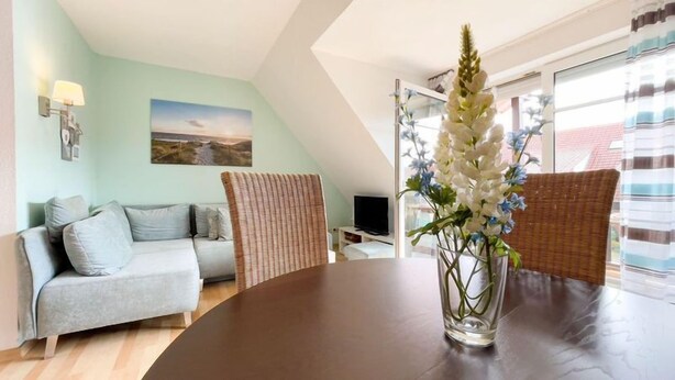 A modern living room with a grey sofa, wicker chairs, a glass coffee table, and a painting on the wall. - Ebbe und Flut, Hannoversche Straße 17 OG, 27476 Cuxhaven- Sahlenburg (Cuxhaven- Sahlenburg)