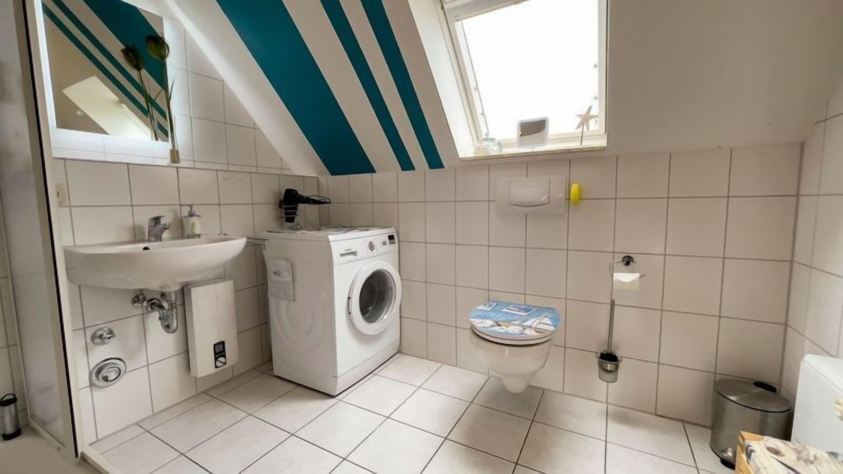 Une petite salle de bain moderne équipée d’un lave-linge, d’un évier et de toilettes.