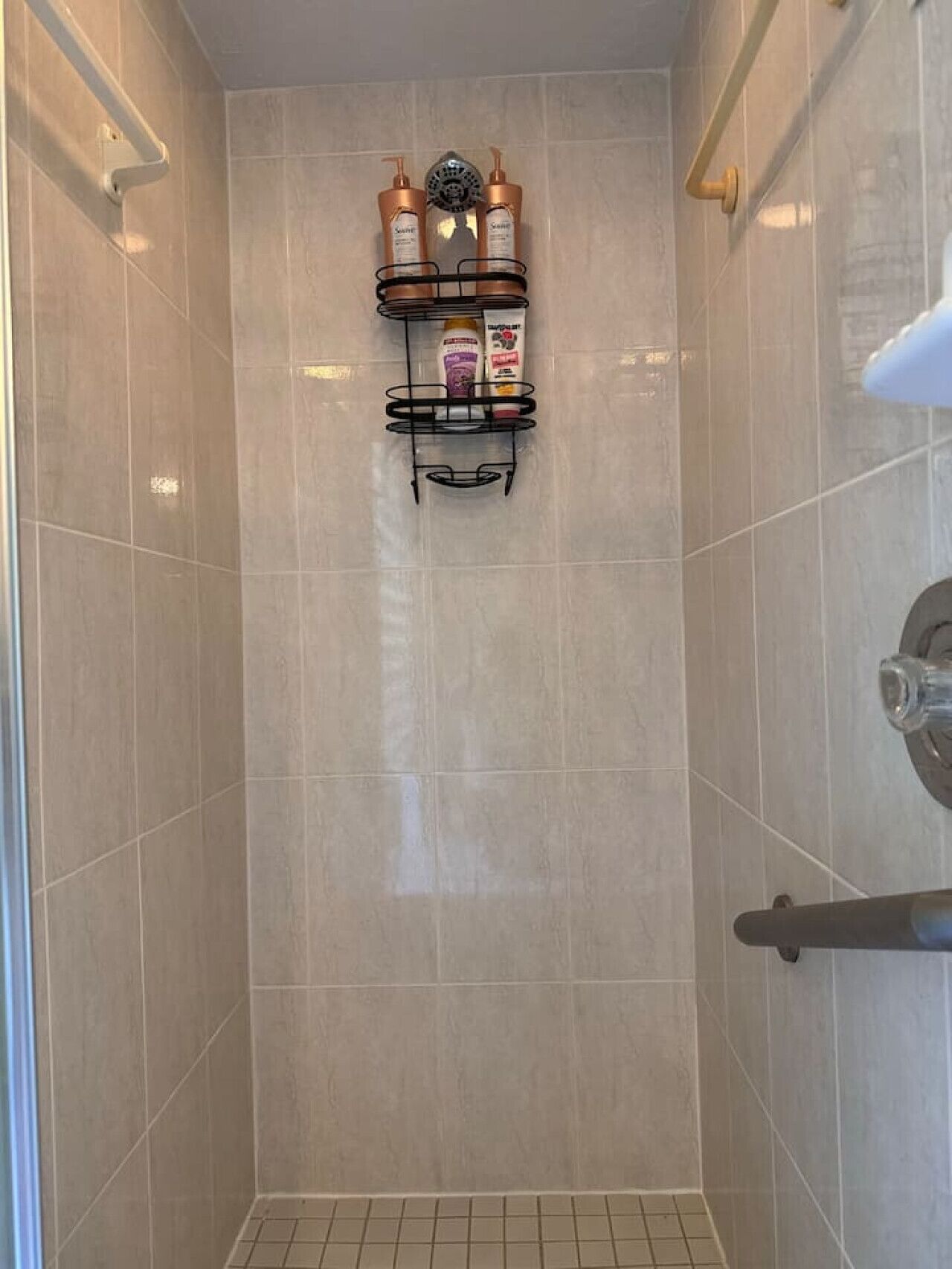 A shower area with beige tiles, a black towel rack with toiletries, and a showerhead.