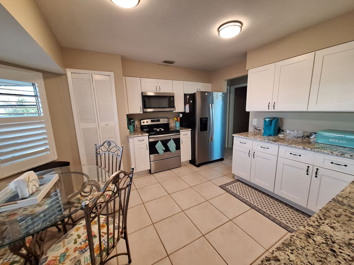 A compact kitchen with white cabinets, stainless steel appliances, and a dining area with a glass table and chairs.