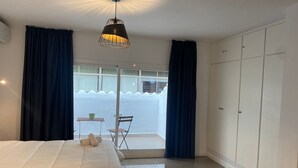 Une chambre à coucher avec un lit, une petite table et une chaise, une armoire et une vue sur la mer par la fenêtre.