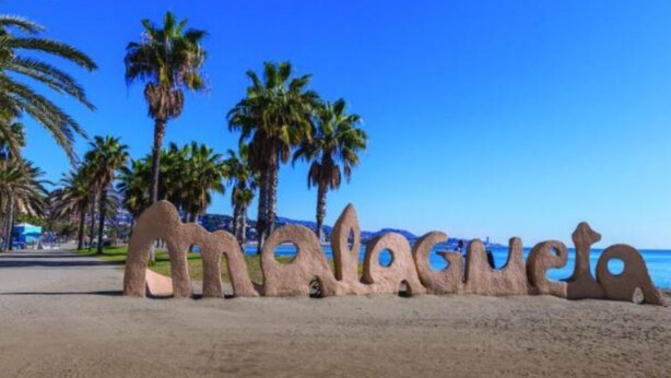 Une plage de sable bordée de palmiers et sur laquelle se trouve une grande sculpture formant le mot « Malaga ».