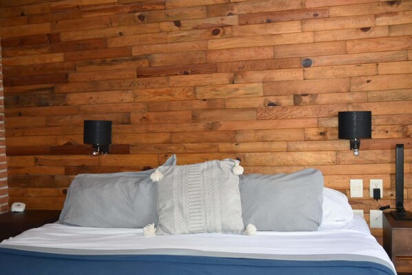 A bed with gray bedding, two wall-mounted lamps, and a wooden wall.