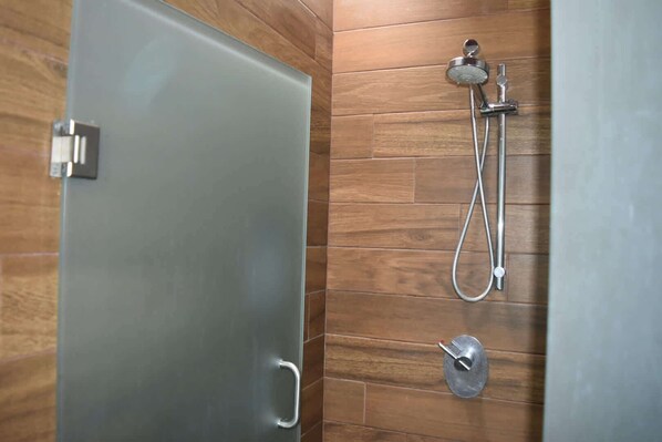 Une salle de bain dotée d’une porte en verre, de carreaux de mur en bois, d’une douche avec un pommeau de douche à main et d’un bidet portatif.
