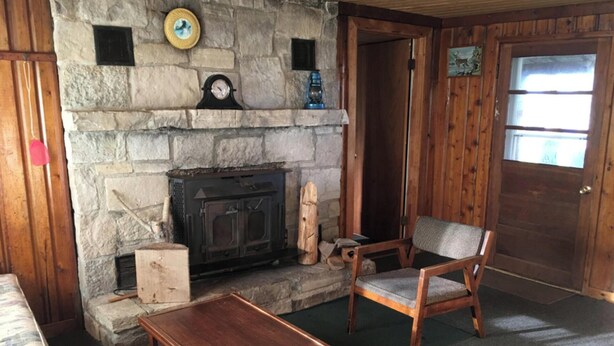 Una chimenea de piedra con un reloj, una puerta de madera y un sillón en una habitación con piso de madera.