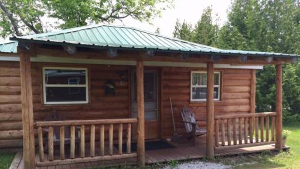 Eine Blockhütte mit Veranda, Tür und Fenstern.