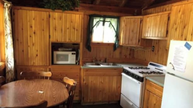 A wooden cabin kitchen with a stove, microwave, sink, and a dining table with chairs.