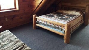 Ein kleiner, hölzerner Raum mit schrägem Dach, einem Einzelbett mit gemustertem Bettbezug und einem Fenster, das für natürliches Licht sorgt.