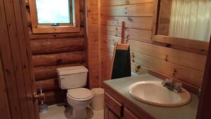 Ein kleines Badezimmer in einer Holzhütte mit Toilette, Waschbecken und Fenster.