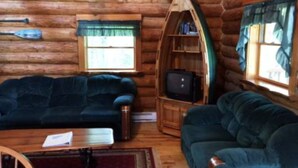 Ein rustikaler Innenraum einer Blockhütte mit einer Couch, einem Fernseher und einem kleinen Bücherregal.