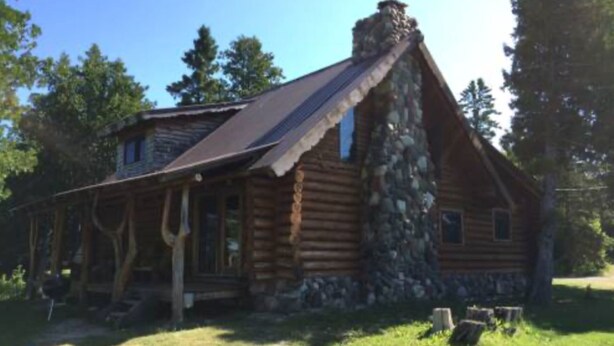 Eine Blockhütte mit Steinofen, einer Veranda und einem Rasen.