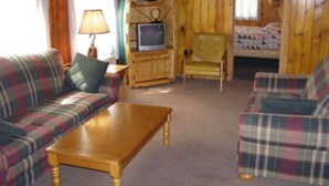 A cabin interior with a plaid sofa, a wooden table, a television, and a yellow chair.