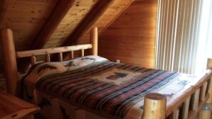 A wooden bed with a patterned bedspread in a room with sloped wooden ceilings.