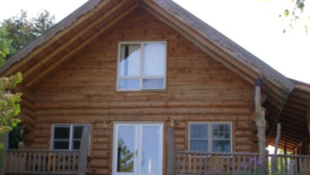 A wooden cabin with a porch, a front door, and a small window above the door.