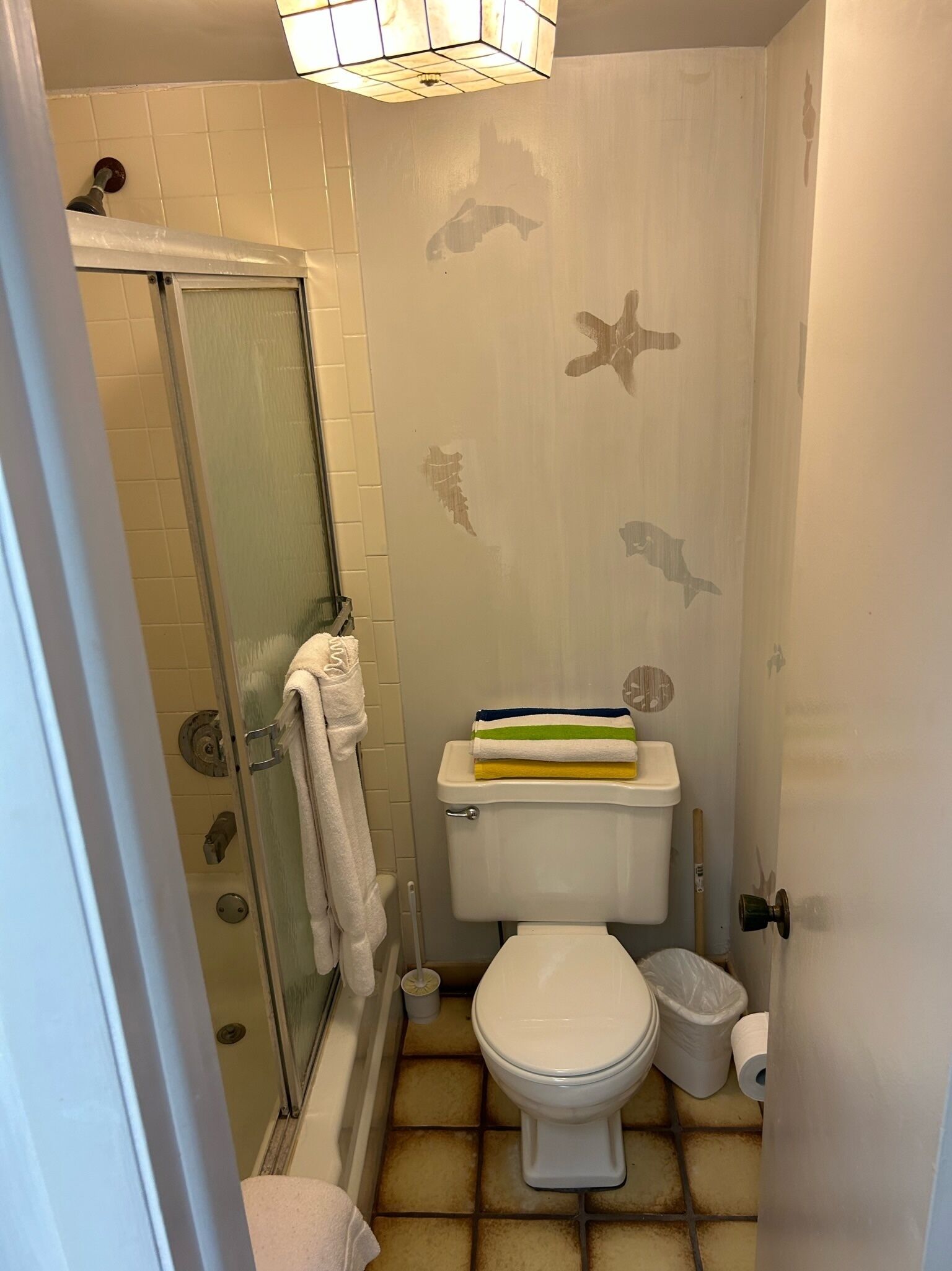 Un baño con cabina de ducha de vidrio, un inodoro con una pila de toallas y un dispensador de papel higiénico.
