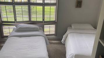 A room with two beds, a window with blinds, and a small picture on the wall.