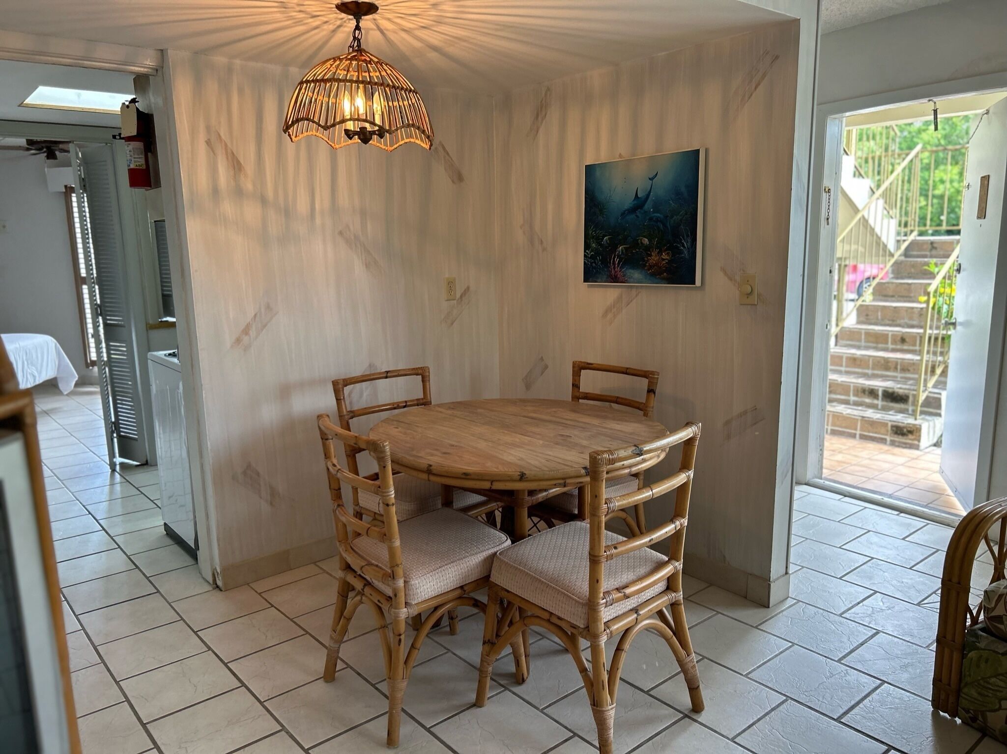 Zona pranzo con tavolo rotondo in legno e quattro sedie in vimini, una lampada a sospensione e un quadro appeso al muro.