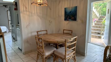 Zona pranzo con tavolo rotondo in legno e quattro sedie in vimini, una lampada a sospensione e un quadro appeso al muro.