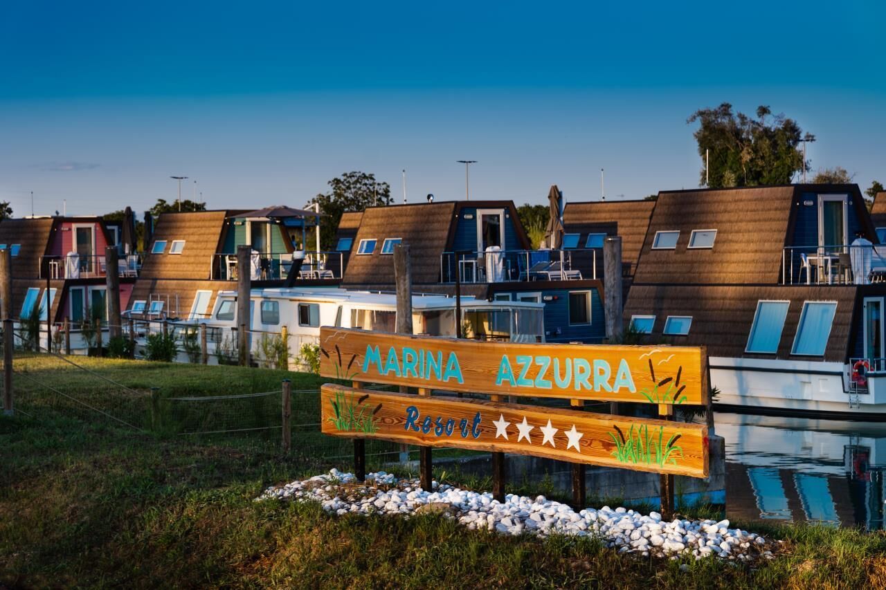 A marina with wooden boat houses and a sign indicating 'Marina Azzurra Resort'.