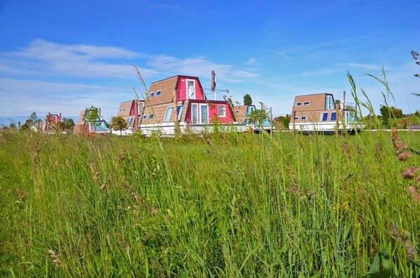 En rad moderna, tvåvåningshus med ett platt tak, belägna på en gräsklädd åker under en klarblå himmel.