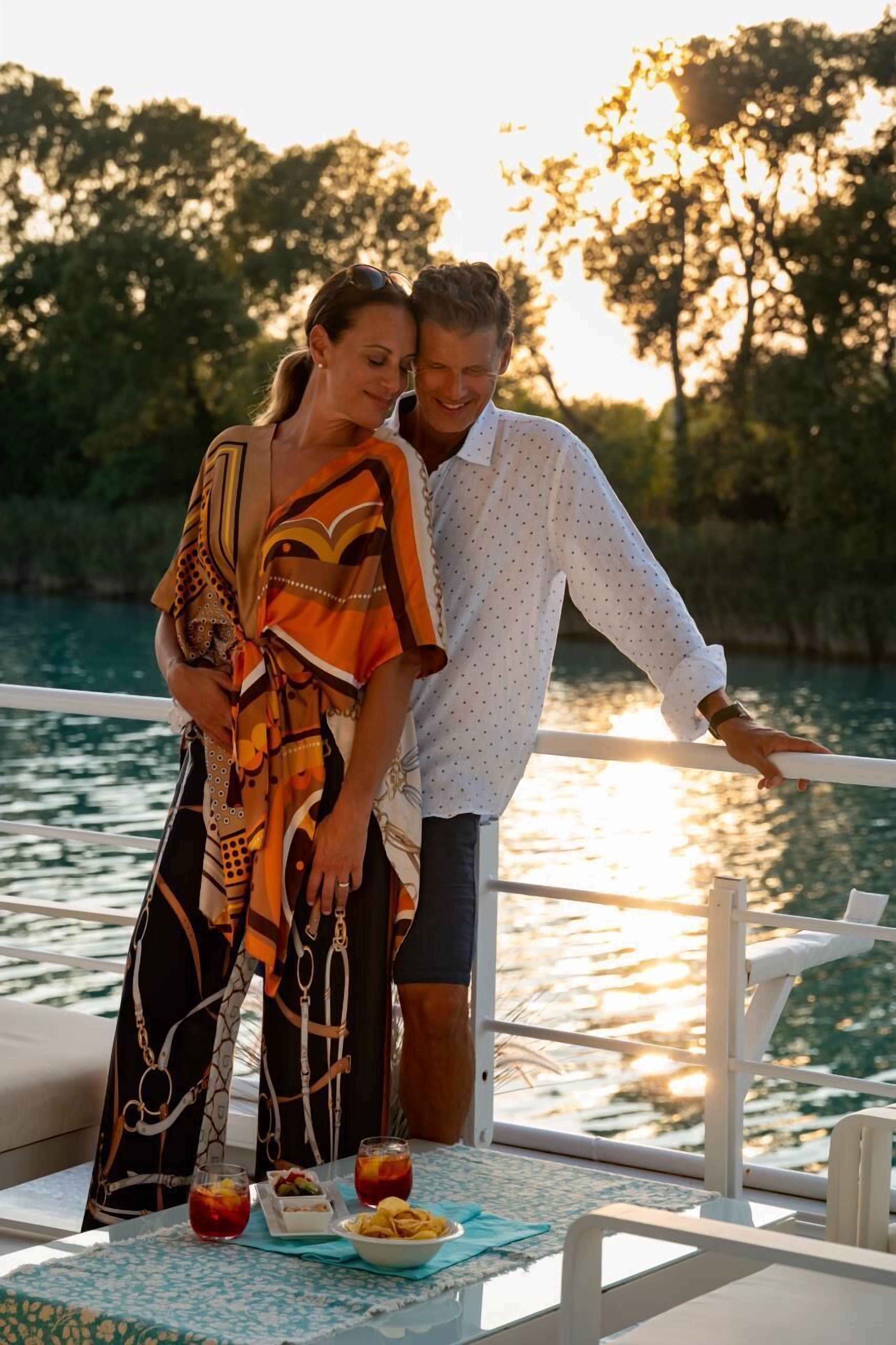 A couple on a boat with a table set with drinks and snacks.