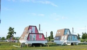 Två moderna, båtformade hus med platta tak och stora fönster, belägna på en gräsklädd yta med träd i bakgrunden.