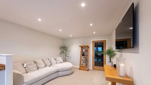 A modern living room with a curved sofa, a wooden side table, a bookshelf, and a TV mounted on the wall. - *Penthouse Luxury Apartment 2min to Carlisle City (Carlisle)