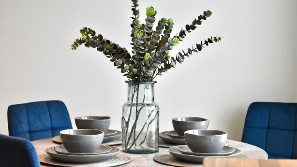 A dining table with a glass vase containing green foliage, surrounded by grey bowls and plates. - *Penthouse Luxury Apartment 2min to Carlisle City (Carlisle)