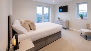 A bedroom with a bed, a TV mounted on the wall, a dresser, and a chair. - *Penthouse Luxury Apartment 2min to Carlisle City (Carlisle)