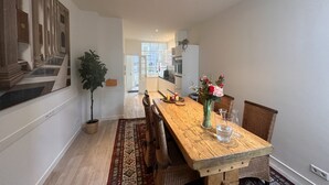Un vaste espace dédié à la salle à manger, avec une longue table en bois, des chaises en osier, une plante en pot et un vase rempli de fleurs.